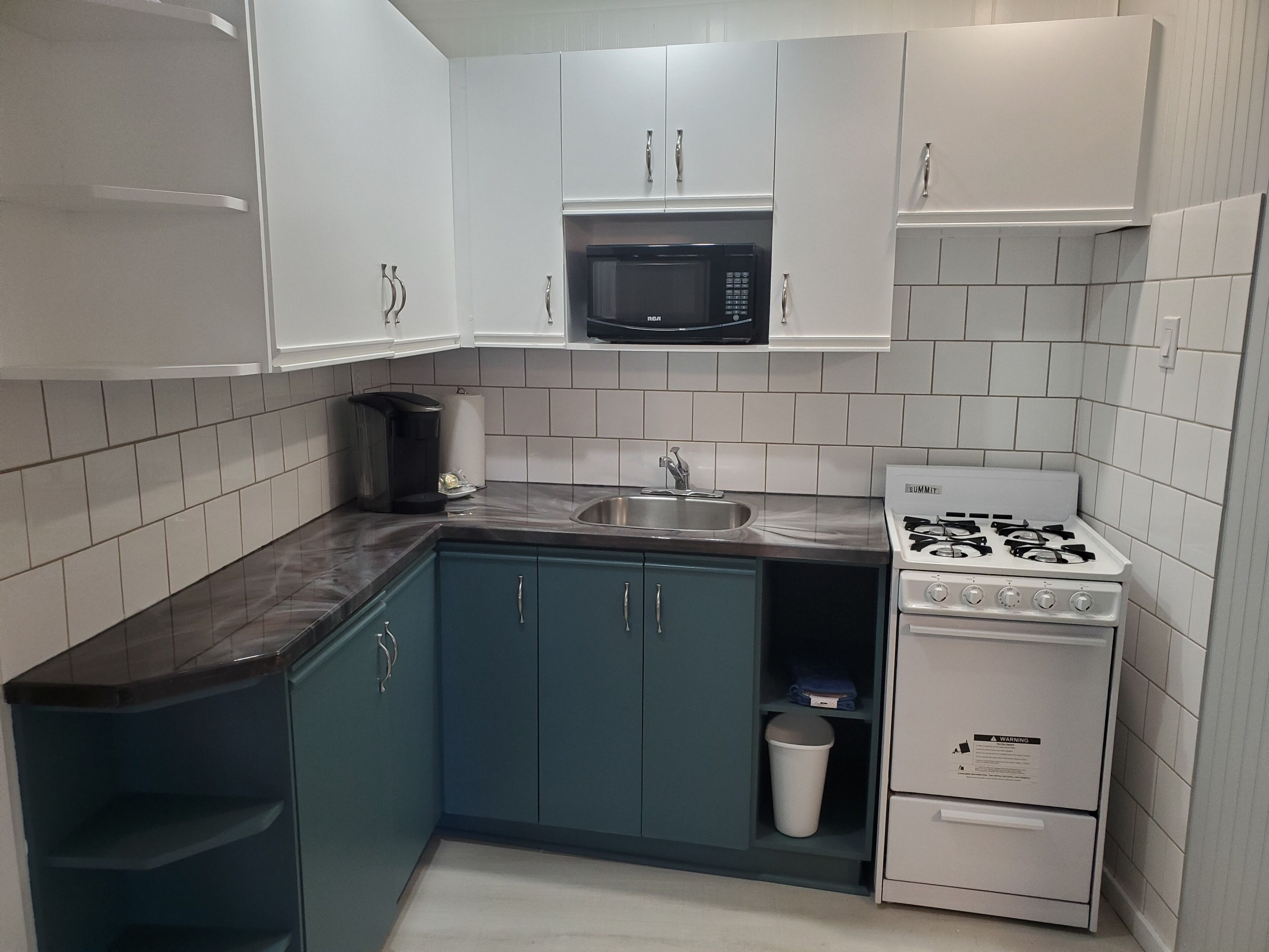 A compact kitchen with white cabinets, a black microwave, a gas stove, and a stainless steel sink.