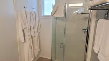 Une salle de bain avec une douche à parois de verre, des toilettes et un lavabo. Des serviettes et des peignoirs blancs sont suspendus à des crochets.