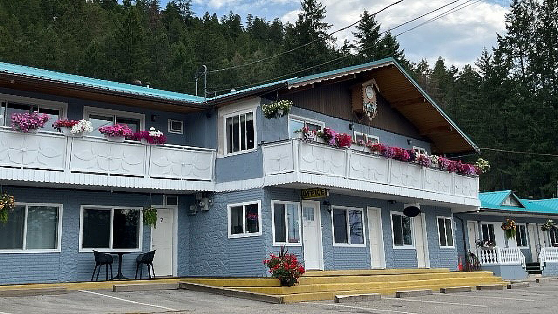 A two-story building with a blue exterior, a wooden front porch, and flower boxes on the balconies.