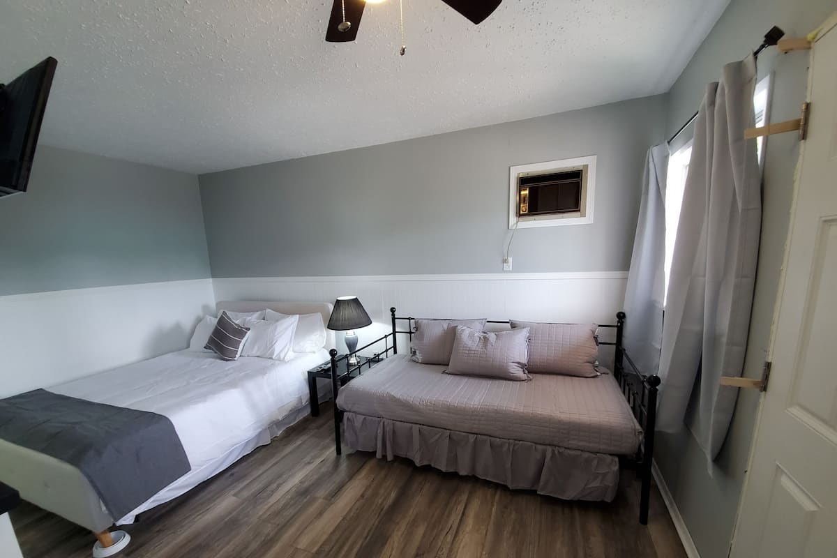A room with two single beds, a small bedside table with a lamp, a window with curtains, and a ceiling light fixture.