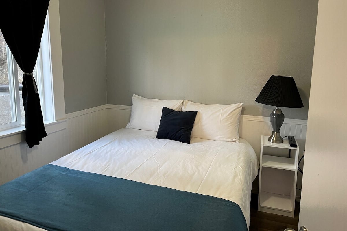 A bedroom with a bed, a nightstand, a lamp, and a window with curtains.