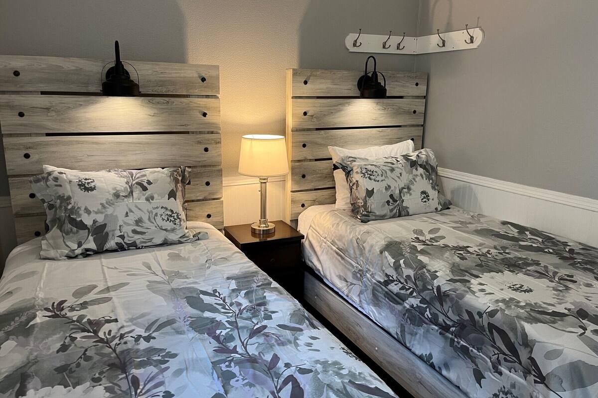 A bedroom with two beds, a nightstand with a lamp, and a coat rack on the wall.