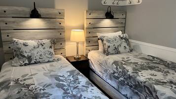 A bedroom with two beds, a nightstand with a lamp, and a coat rack on the wall.