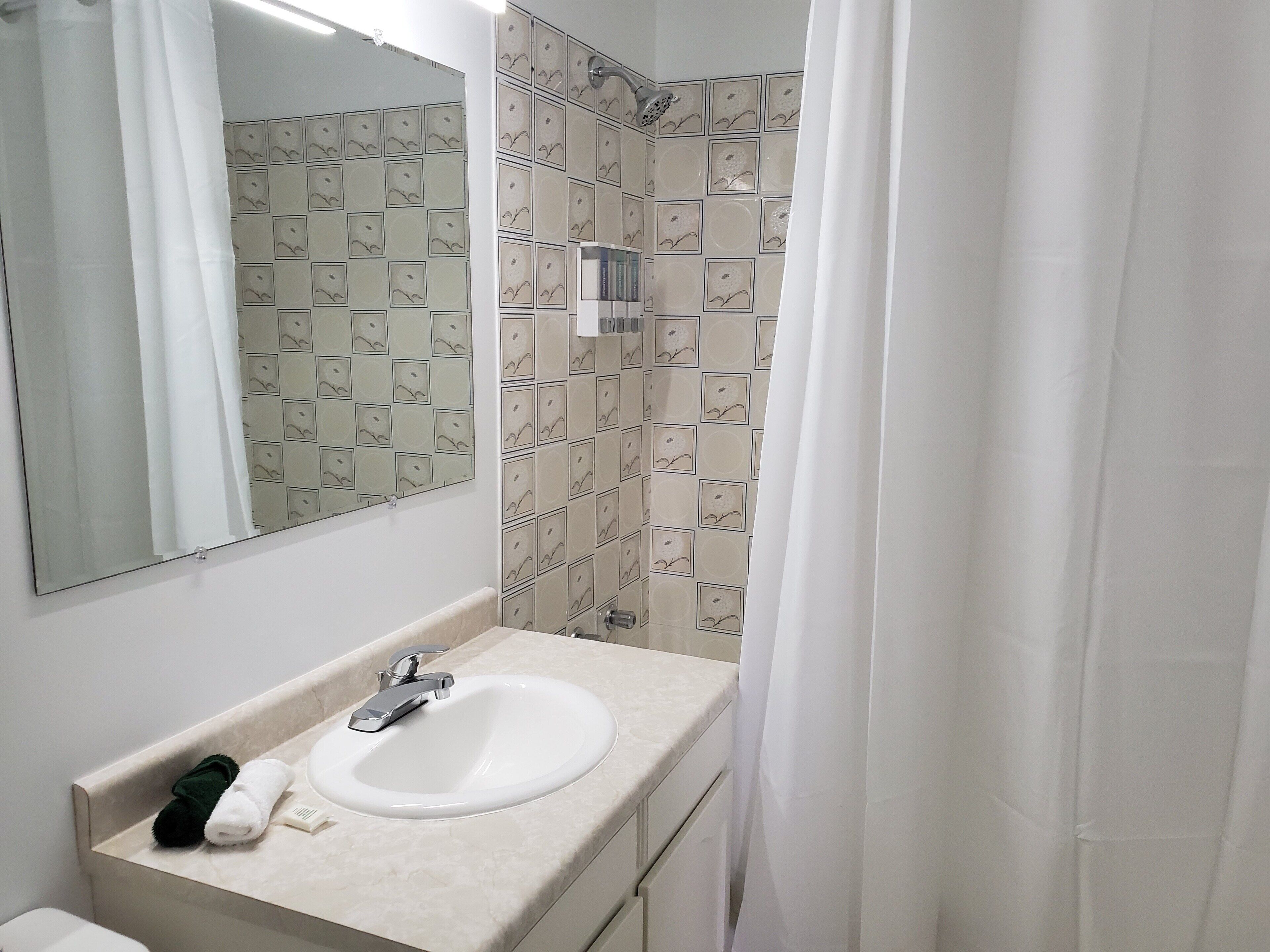A bathroom with a white sink, a mirror, and a shower area with patterned tiles.