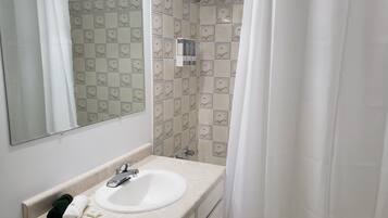 A bathroom with a white sink, a mirror, and a shower area with patterned tiles.