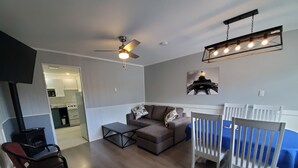 Una sala de estar con un sofá, una mesa de centro, una silla blanca, un ventilador de techo y un accesorio de luz montado en la pared.