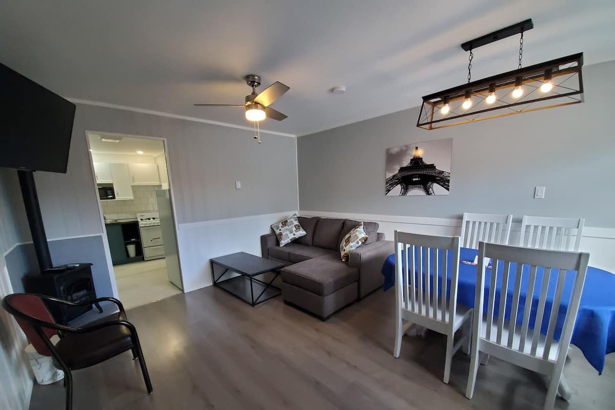 A living room with a sofa, a coffee table, a white chair, a ceiling fan, and a wall-mounted light fixture.