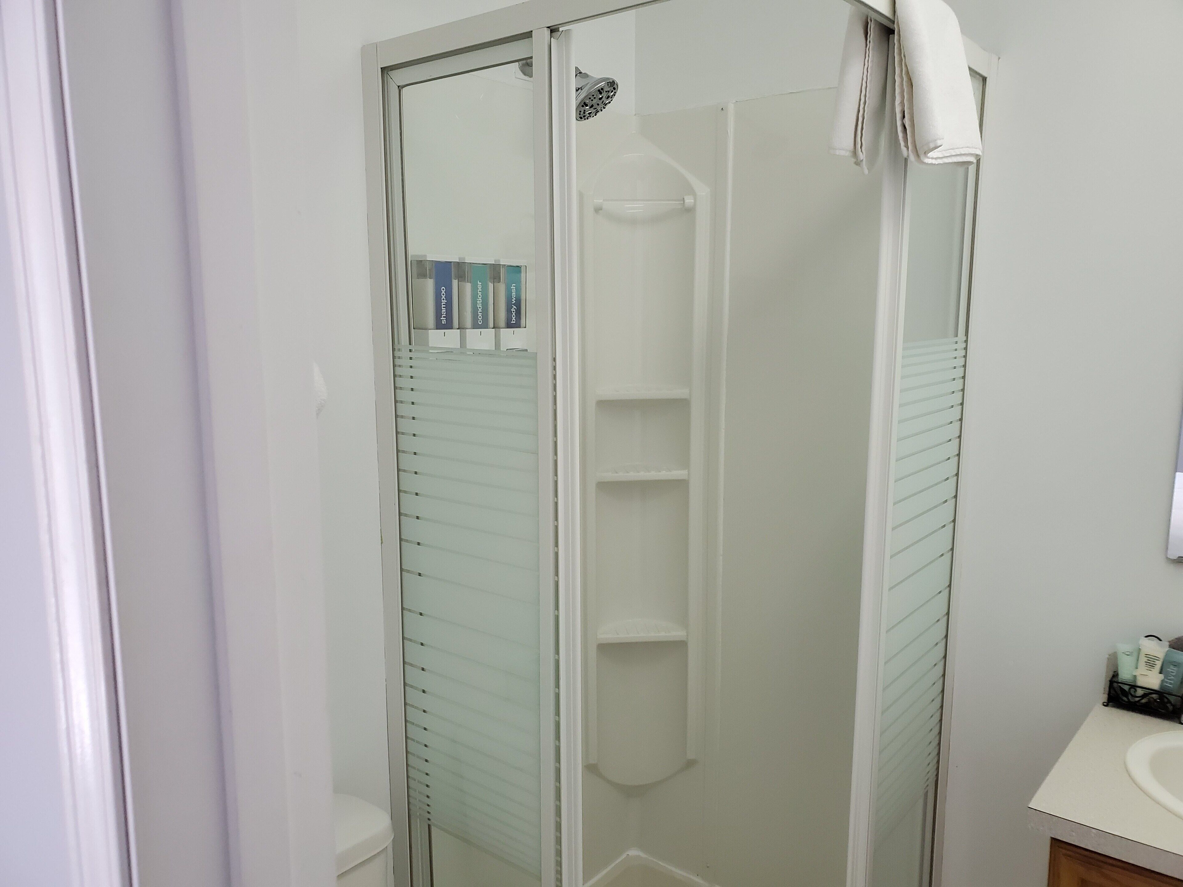 Un baño moderno con ducha de vidrio, lavamanos blanco y toallero.