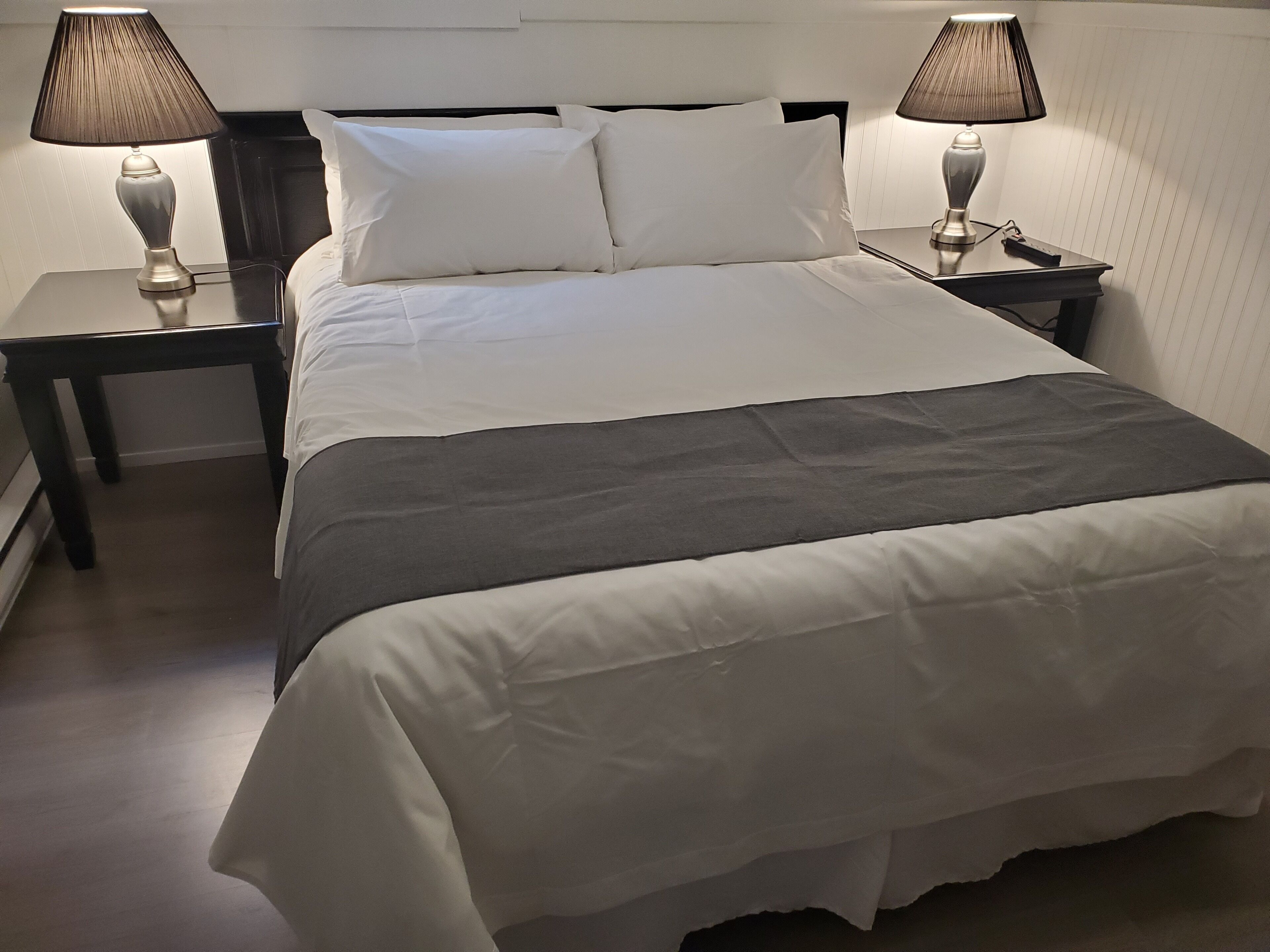 A neatly made bed with white linens and a gray throw blanket, flanked by two bedside tables with lamps.