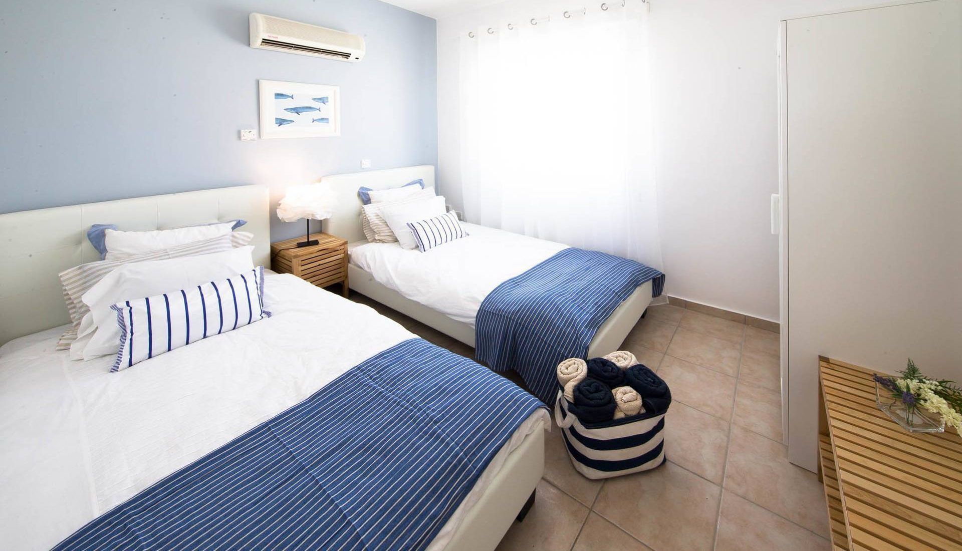 Habitación de hotel con dos camas, una mesita de noche, una pequeña mesa con un florero y un equipo de aire acondicionado en la pared.