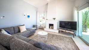 A modern living room with a grey sofa, a white coffee table, a fireplace, and a TV. - Villa Luna (Pegeia)