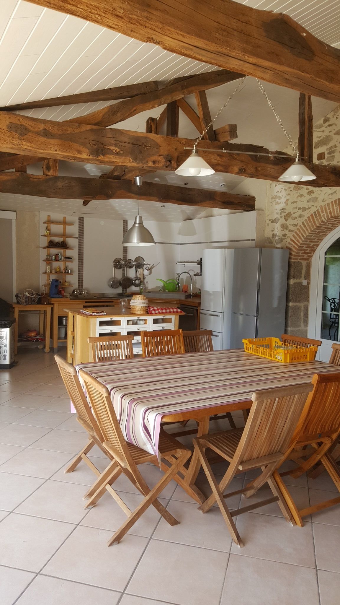 A rustic kitchen with exposed wooden beams, a dining table with chairs, and a refrigerator.
