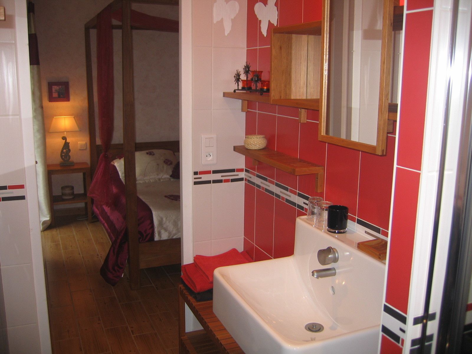 Un bany d'hotel amb un envàs blanc, parets revestides de rajoles vermelles, una panxa de fusta i un llit al fons.