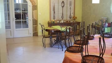 Un comedor con techo alto, vigas de madera a la vista y suelo de baldosas. Hay varias mesas con sillas, un menú colgado en la pared y una puerta que da a otra habitación.