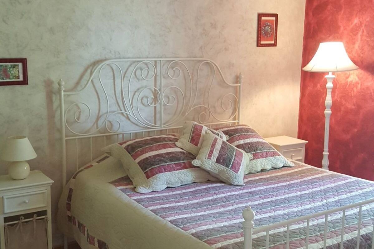 Un dormitorio con estructura de cama de metal blanco, colcha acolchada y pared de acento roja.