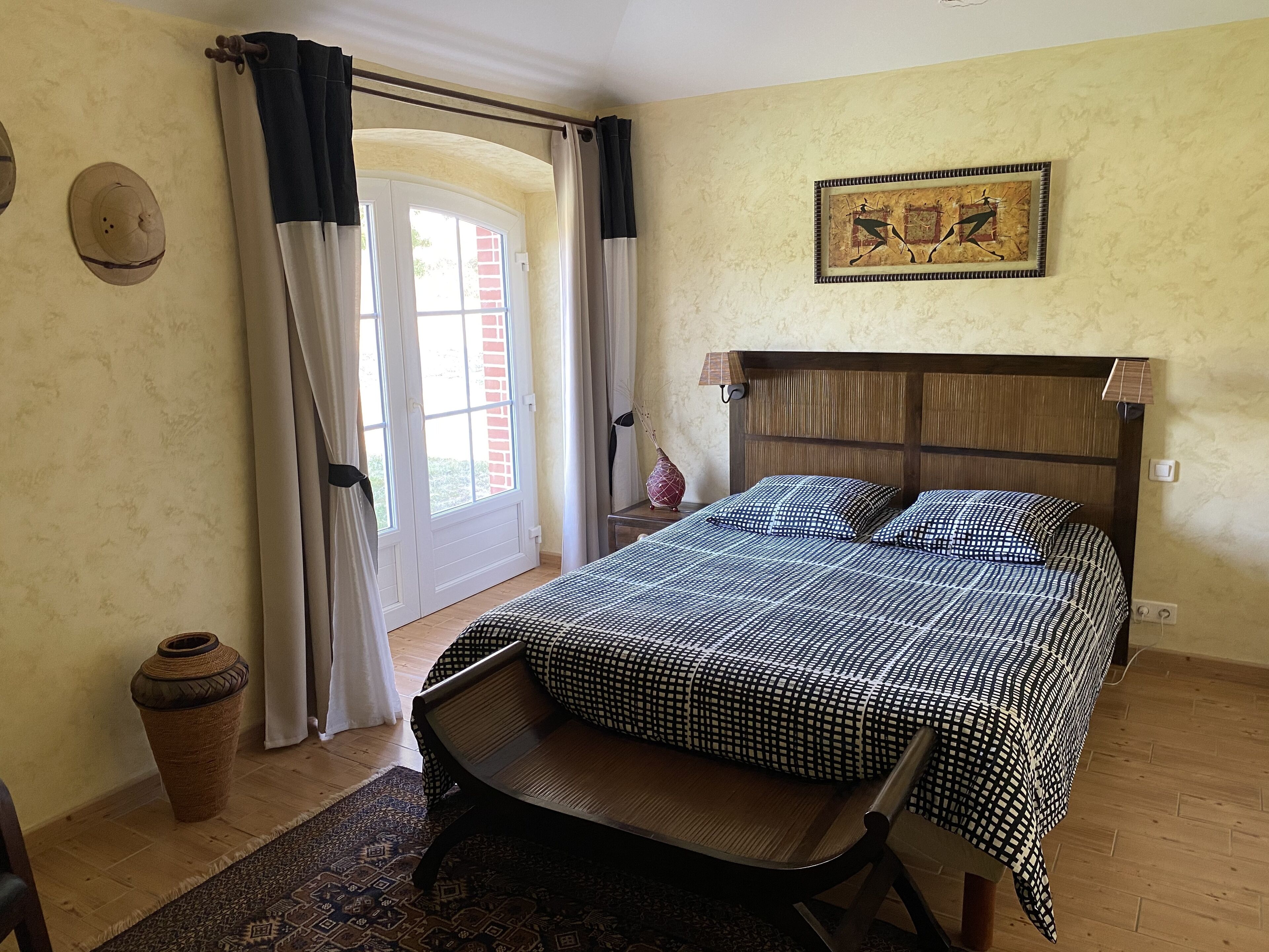 Un dormitorio con una cama, una silla, una lámpara, un florero y una puerta que da a un espacio exterior.