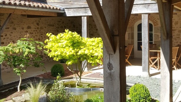 Eine Pergola aus Holz mit Steinmauern und einem Gartenbereich mit verschiedenen Pflanzen und einem kleinen Teich.