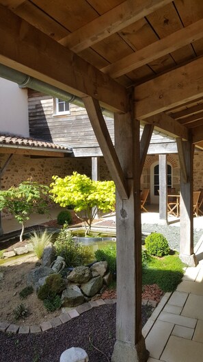 Une structure de pergola en bois, avec des murs en pierre et un espace jardin agrémenté de diverses plantes et d’un petit étang.