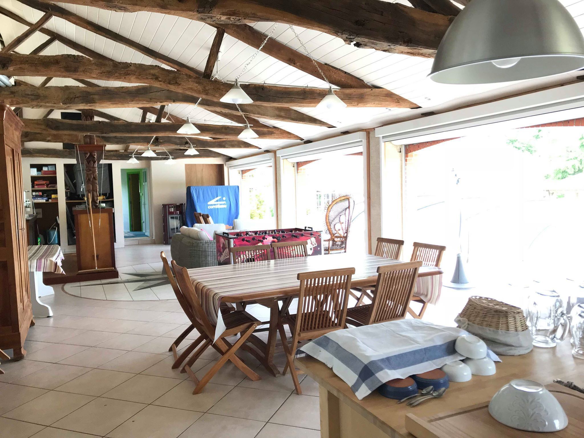 Uma sala de jantar ampla com mesa e cadeiras de madeira, uma mesa de futebol e uma grande janela que oferece luz natural.