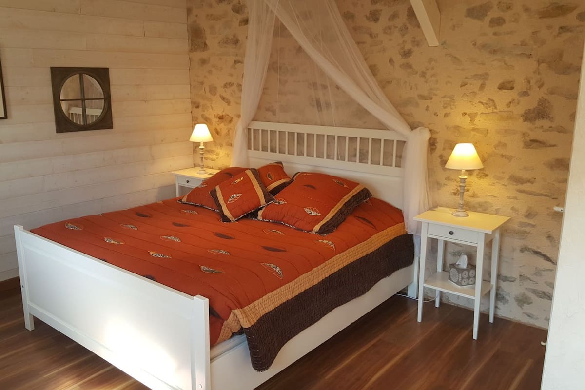 Un dormitorio con una cama blanca, una colcha roja y dos mesitas de noche con lámparas.