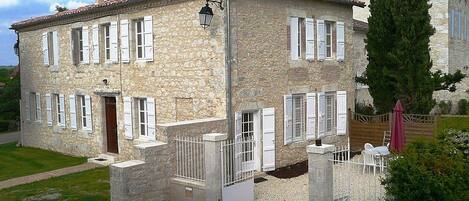 A stone building with a tiled roof, white shutters, and a gated entrance.