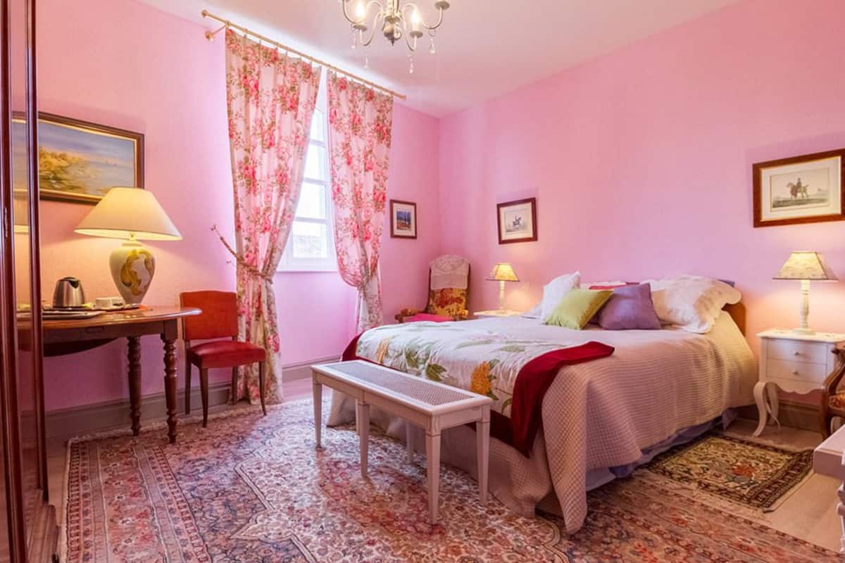 A pink-themed bedroom with a bed, bedside tables, a chair, a desk, and a chandelier.