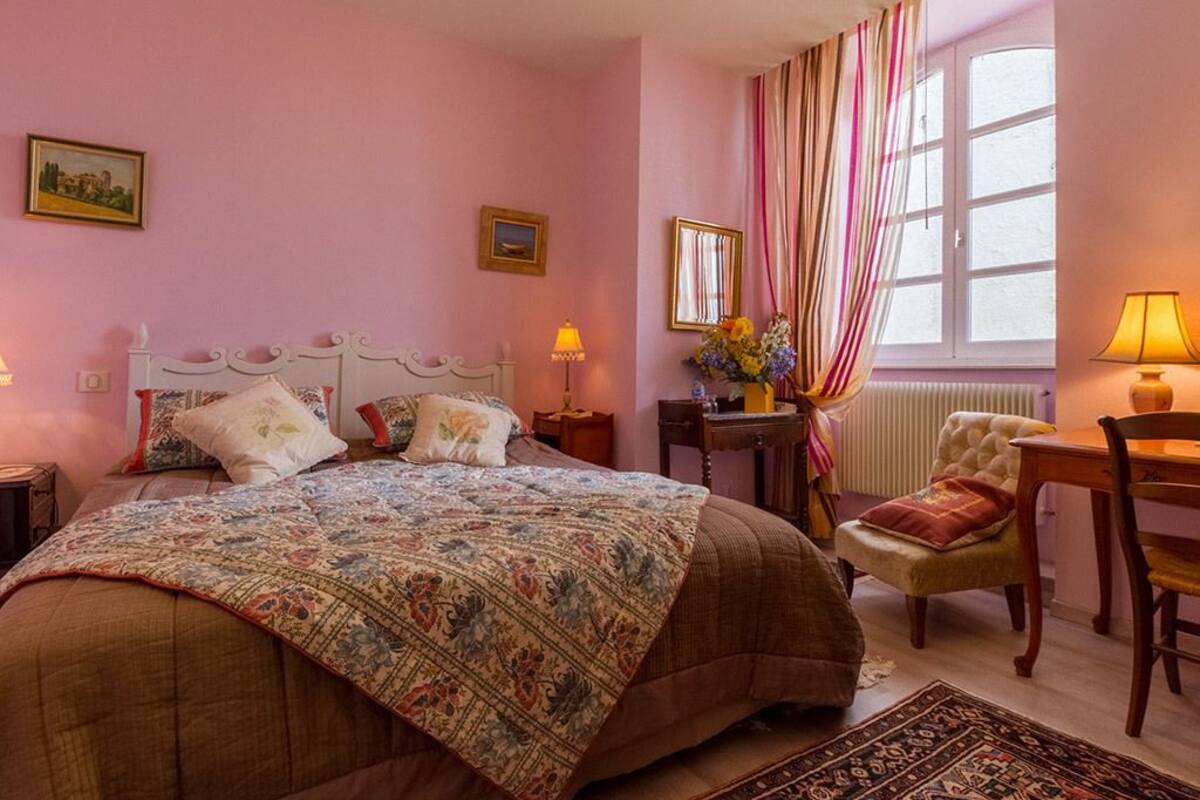 A bedroom with a large bed, a chair, a table, and a window with curtains.