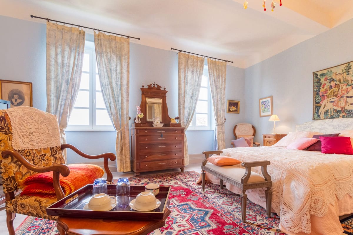 A traditional bedroom with a bed, a wooden dresser, a chair, and a tray with teacups.