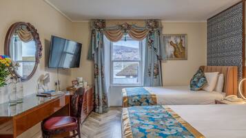 Ett hotellrum med ett skrivbord, en stol, två sängar, en TV, en stor spegel och ett fönster med gardiner.