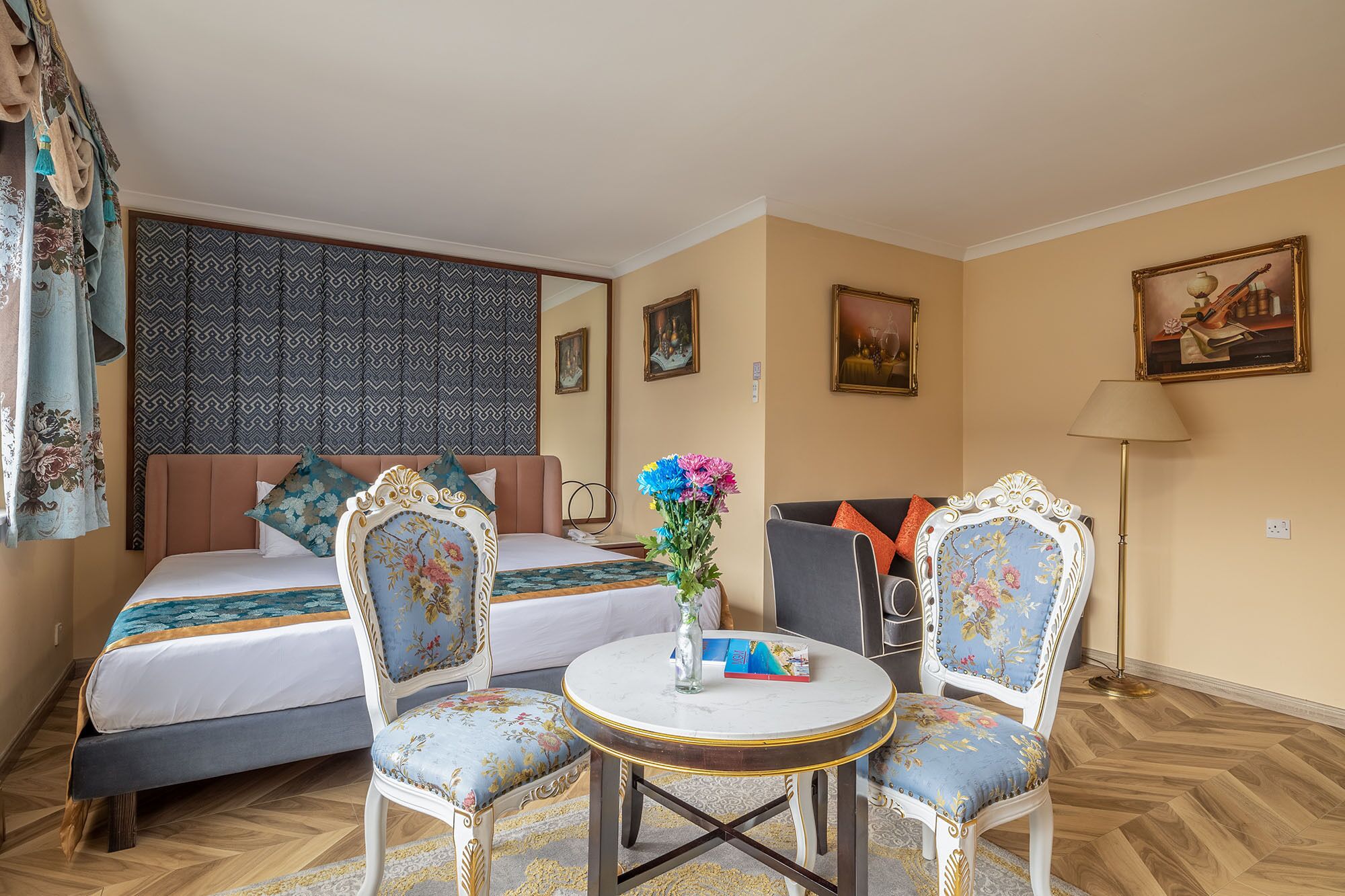 A hotel room with a bed, two upholstered chairs, a small round table, and a vase with flowers.