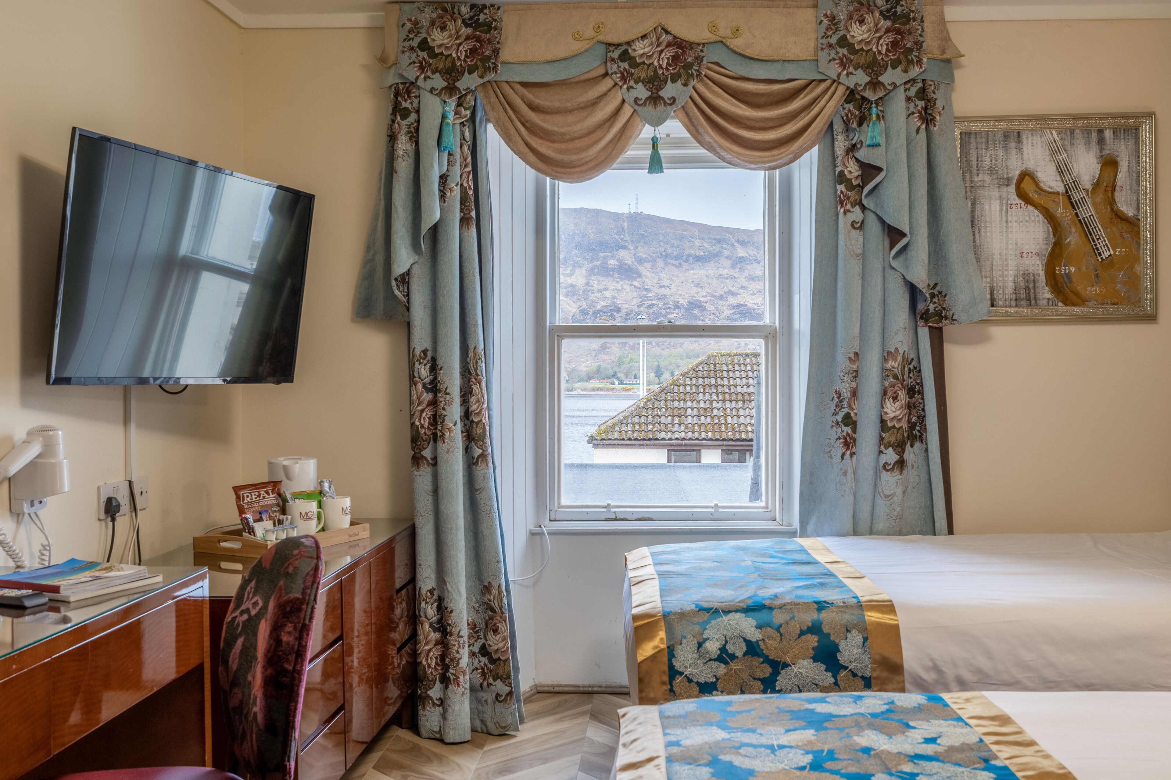 A hotel room with a bed, a desk with a computer, a TV, and a window with curtains.