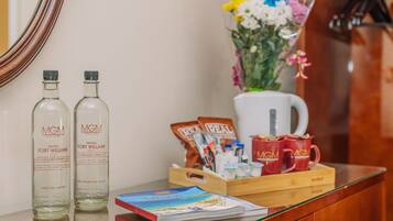 A hotel reception area with two bottles of water, a coffee maker, a tray with coffee packets, a vase with flowers, and a magazine on the counter.