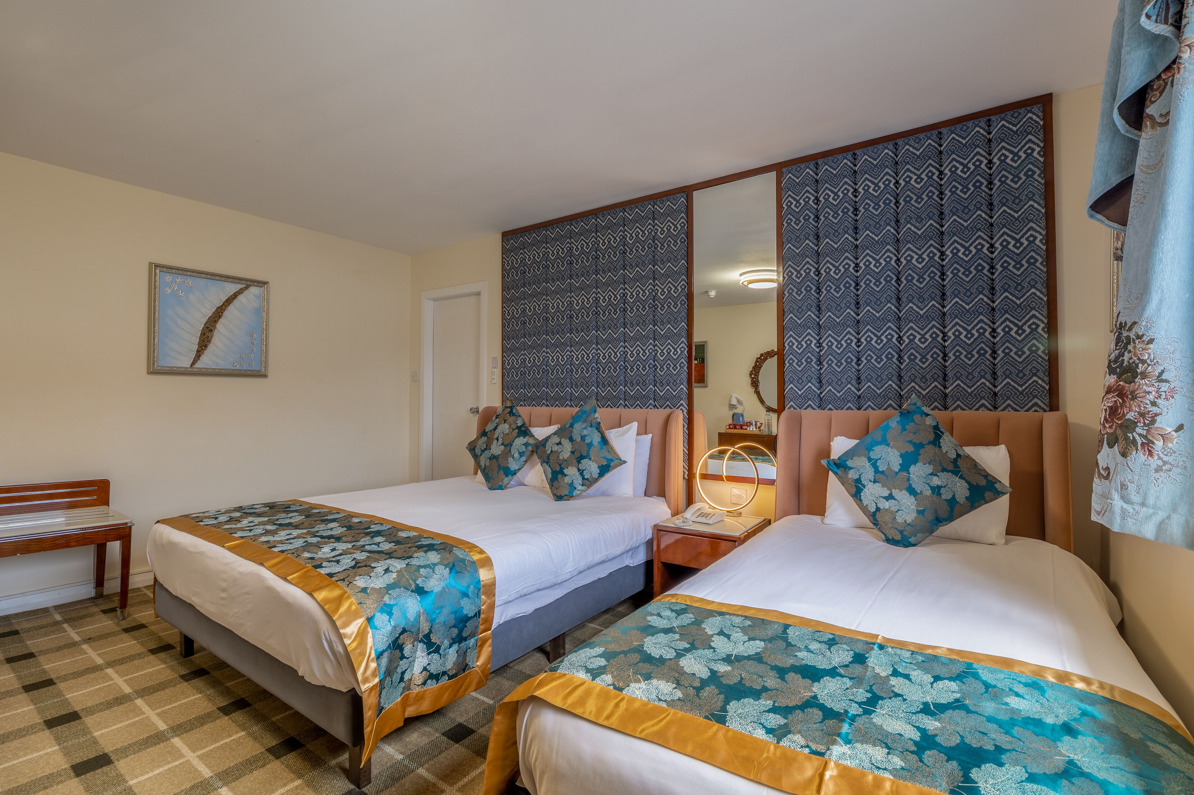 Een hotelkamer met twee bedden, een bankje, een receptiebalie en een spiegel.