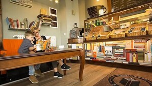 A cozy bookstore with a wooden table, bookshelves, and a coffee machine. - Bett & Buch Hotel (Berlin)