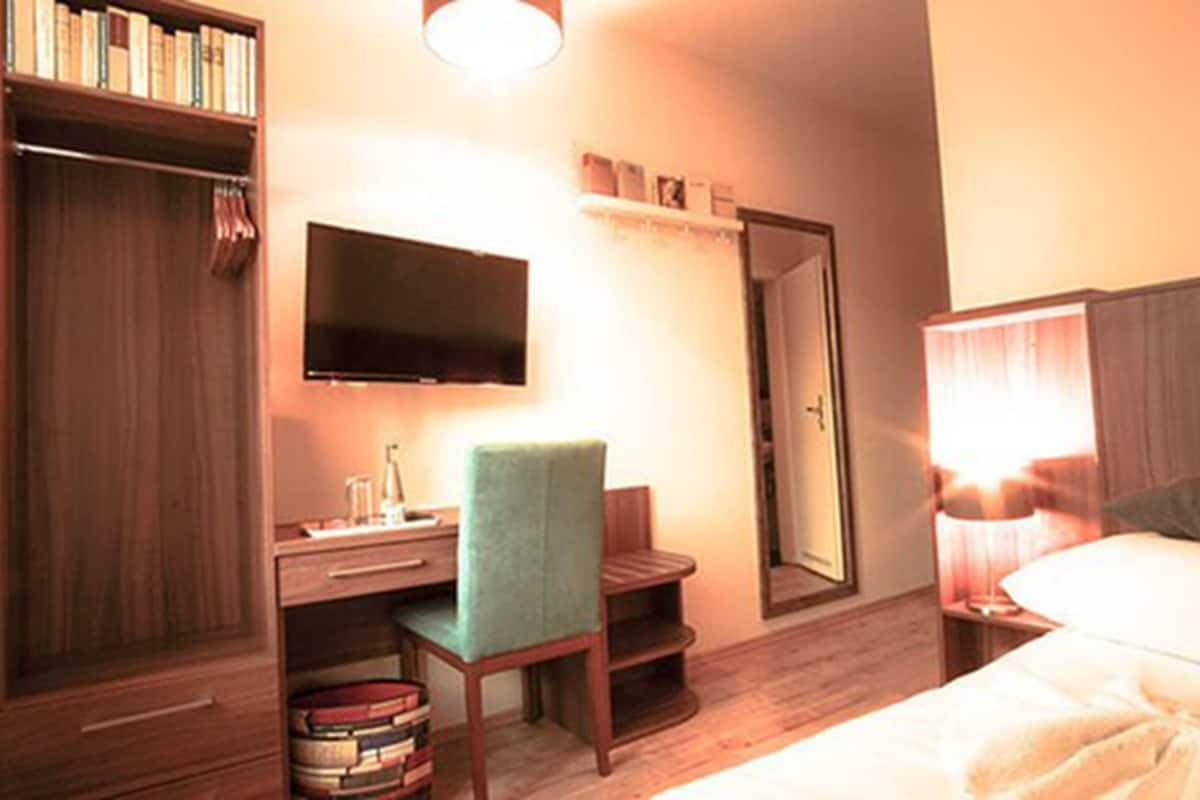 A hotel room with a bed, a desk with a chair, a television, a wardrobe, and a mirror.