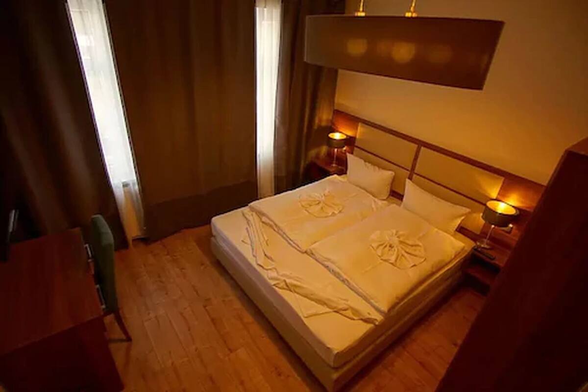 A hotel room with a large bed, two bedside tables with lamps, a wooden floor, and a view of the outdoors through a window.
