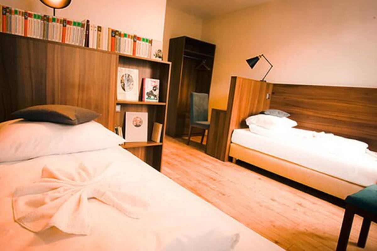 A hotel room with two beds, a bookshelf, a desk, and a chair.