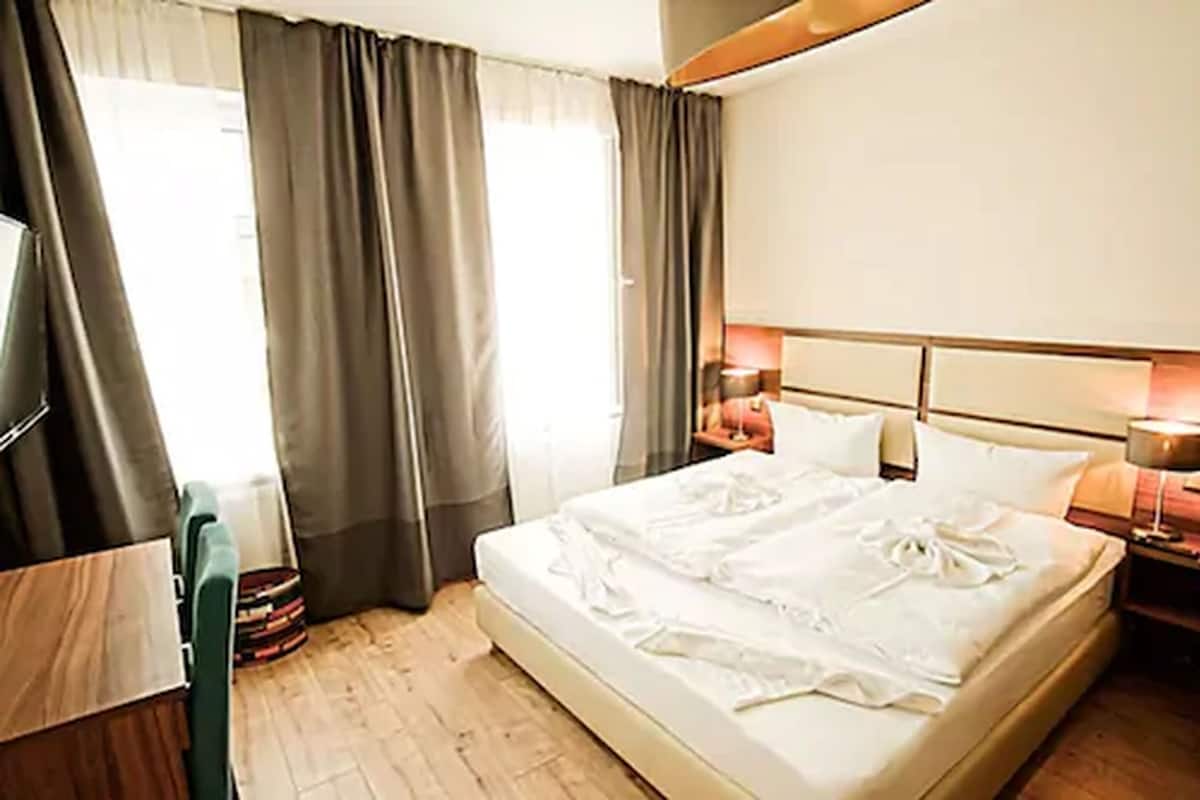 A hotel room with a bed, bedside lamps, a TV, and a window with curtains.