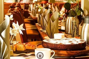 A restaurant setting with neatly arranged tables, a cake on a wooden board, and a coffee cup with a logo. - Bett & Buch Hotel (Berlin)