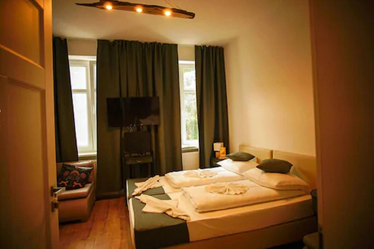 A bedroom with a bed, a TV, a window with curtains, and a small seating area.