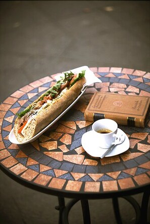 A sandwich on a plate, a cup of coffee, and a book on a table. - Bett & Buch Hotel (Berlin)