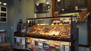 A bakery display case with various baked goods, a chalkboard menu above, and bookshelves below. - Bett & Buch Hotel (Berlin)