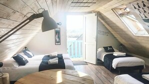 Ein gemütliches Schlafzimmer im Dachgeschoss mit zwei Betten, einem Holztisch und einem großen Fenster mit Blick ins Freie.