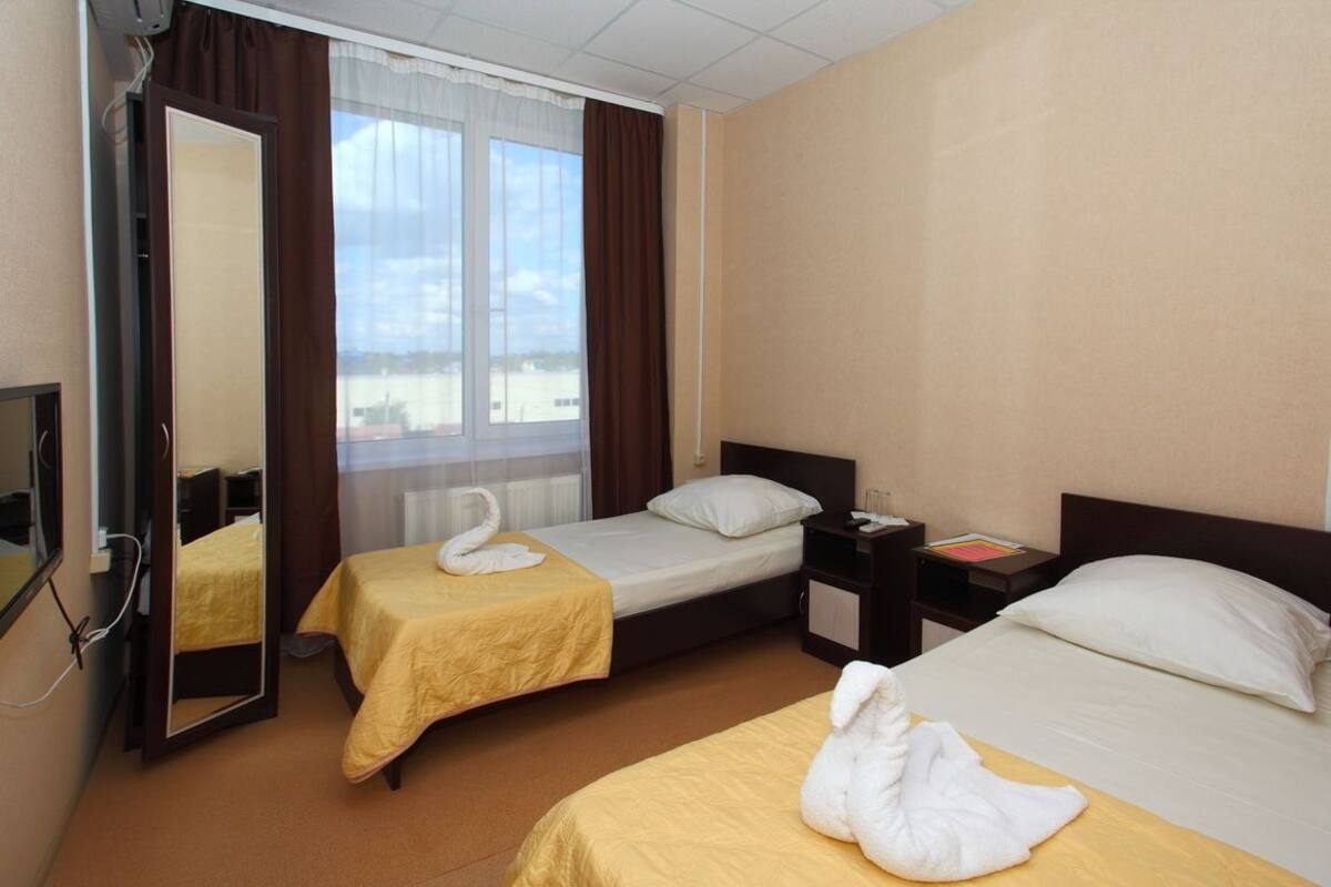 A hotel room with two beds, a mirror, a nightstand, and a window with curtains.