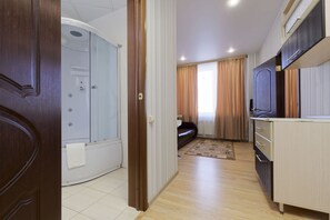 A modern hotel room with a shower, a sofa, a kitchen area, and a view of the city. - Hotel Orion-Apartment (Tver)
