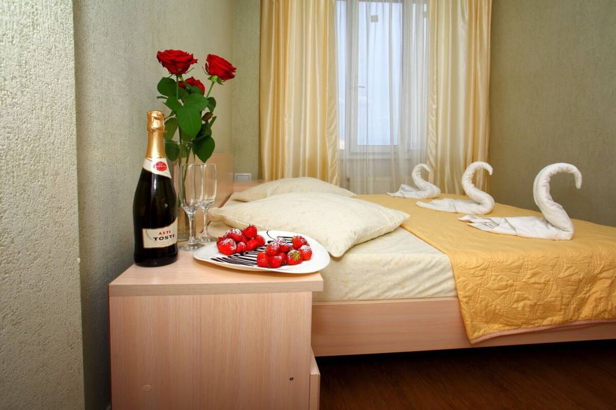 A neatly made bed with a yellow bedspread, a bottle of wine, a glass, and a plate of strawberries on a bedside table.