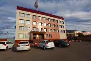 A multi-story building with a red roof and beige walls, featuring a parking lot with several cars. - Hotel Orion-Apartment (Tver)