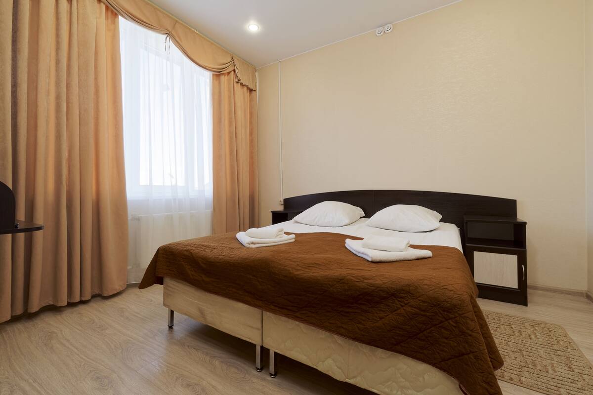 A hotel room with a bed, a nightstand, a TV, and a window with curtains.