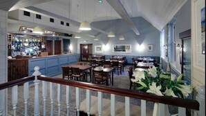 Un restaurant doté d’un bar, de tables et de chaises en bois, ainsi que d’un escalier muni d’une rampe.