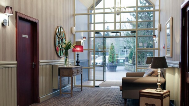 Un hall d’hôtel avec une porte en bois portant l’inscription « Privé », une table ronde ornée d’un vase de fleurs, un canapé et une lampe.
